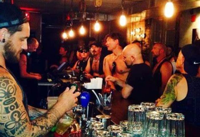 Inside Black Eagle cruising bar, Toronto. Tattooed bartender pours a beer. Gay bar scene with men in leather and casual wear.