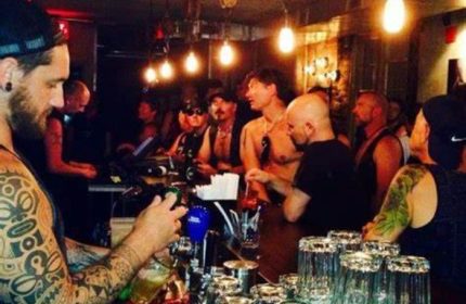 Inside Black Eagle cruising bar, Toronto. Tattooed bartender pours a beer. Gay bar scene with men in leather and casual wear.