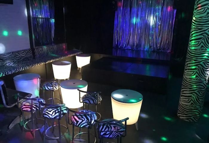 Interior of a gay club in Madrid. Zebra print details, illuminated seating, and a stage with colorful lighting. Black and white decor.