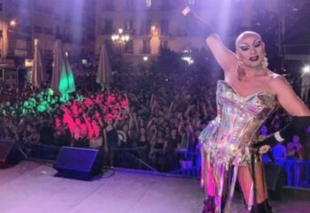 Drag queen on stage at a gay club in Madrid. Crowd with hands up, lights, and energy. Gay travel nightlife scene.