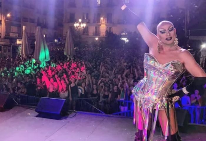 Drag queen on stage at a gay club in Madrid. Crowd with hands up, lights, and energy. Gay travel nightlife scene.