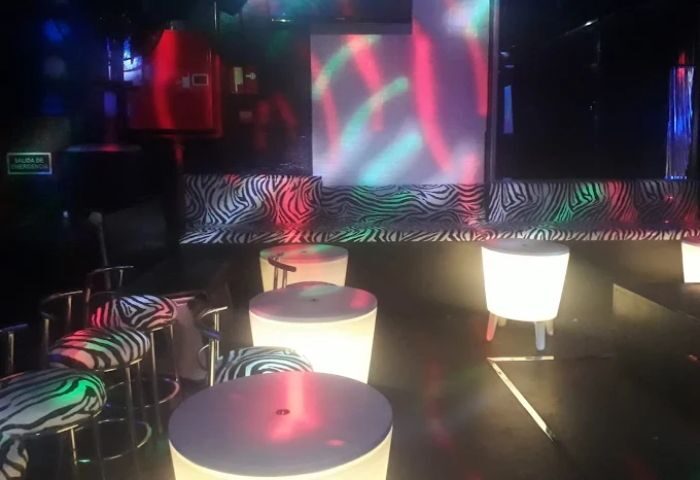 Interior of a black and white gay club in Madrid. Zebra print seating, illuminated tables, and colorful lighting create a vibrant atmosphere.