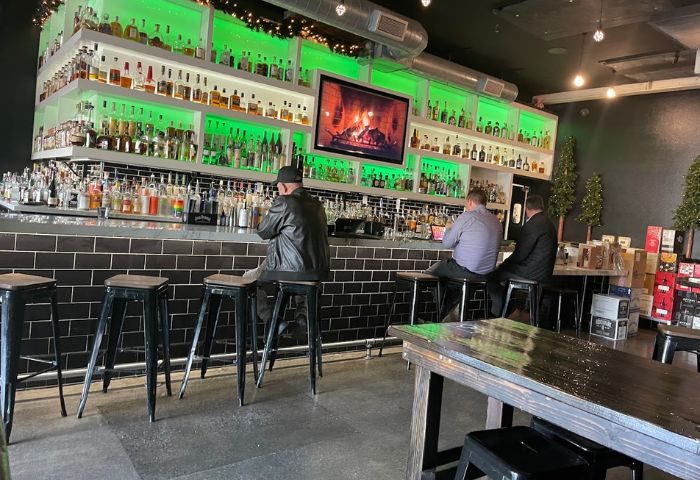 Blackbook Bar interior. Men at bar with liquor shelves, green lighting, & TV. Gay travel advice for nightlife & drinks.