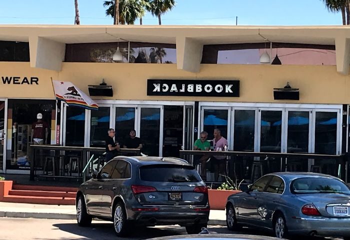 Blackbook location: Exterior view of Blackbook, a gay bar in Palm Springs, California. People at the bar, cars parked in front.