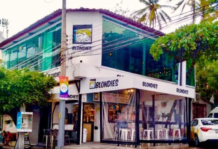 Blondies Loft Slush Bar, a gay party spot in Puerto Vallarta. Two-story building with glass windows, palm trees, & Blondies signage.
