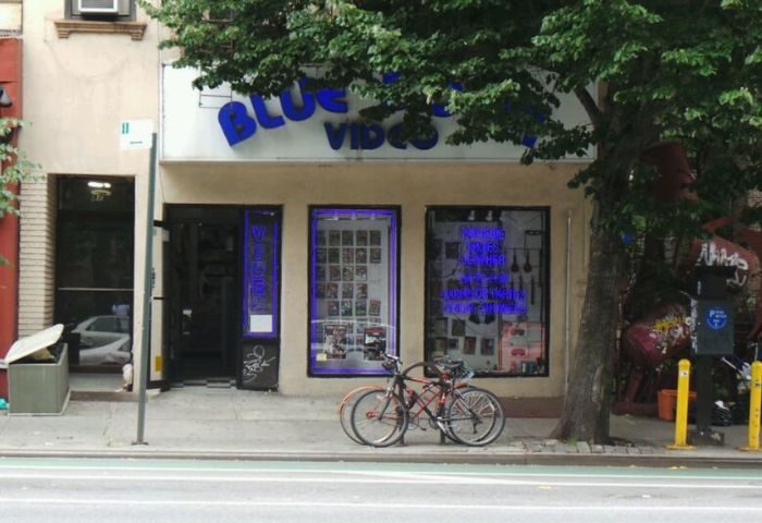 Blue Door Video, a gay sauna in New York. Storefront with blue neon sign. Bicycles parked outside. Gay travel destination.