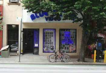 Blue Door Video, a gay sauna in New York. Storefront with blue neon sign. Bicycles parked outside. Gay travel destination.