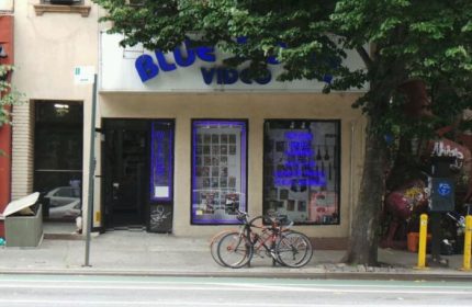 Blue Door Video, a gay sauna in New York. Storefront with blue neon sign. Bicycles parked outside. Gay travel destination.