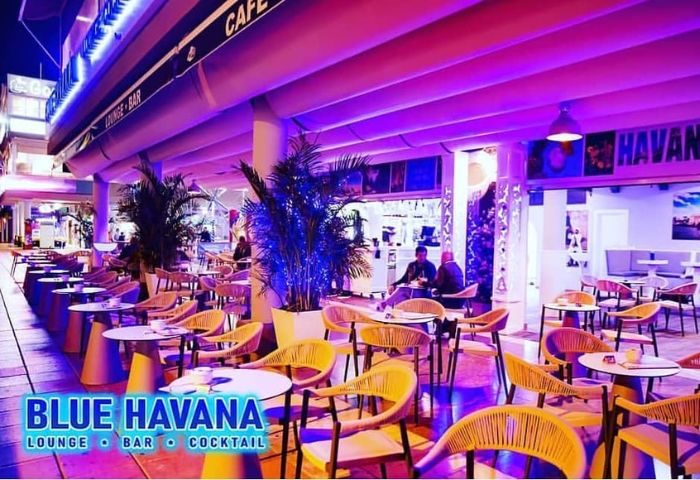 Blue Havana Lounge, a gay bar in Gran Canaria. Outdoor seating area with tables and chairs, illuminated with blue and purple lighting.
