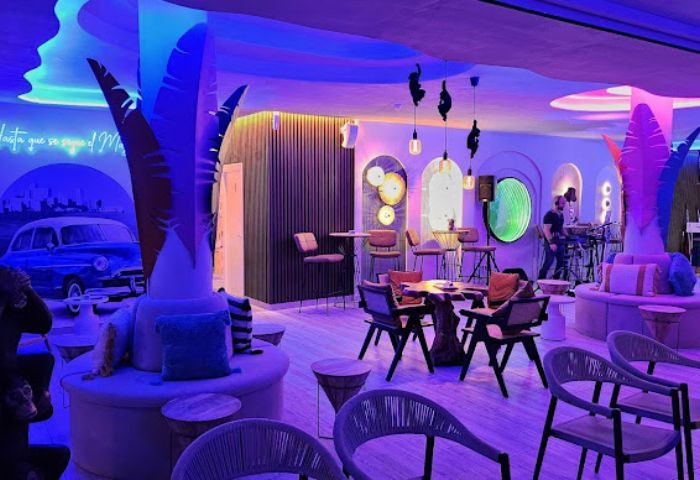 Blue Havana Lounge, a gay bar in Gran Canaria. Stylish interior with palm tree decor, blue lighting, and a classic car mural. Trendy gay nightlife.
