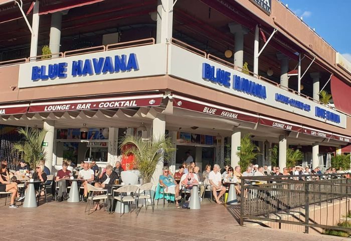 Blue Havana Lounge, a gay bar in Gran Canaria. People sit outside at tables. The bar's name is displayed prominently.