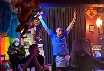 Bobby's Monkey Bar in Key West: A gay man sings karaoke with enthusiasm. Funny meme of Bernie Sanders in the background. Gay travel.