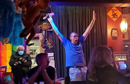 Bobby's Monkey Bar in Key West: A gay man sings karaoke with enthusiasm. Funny meme of Bernie Sanders in the background. Gay travel.