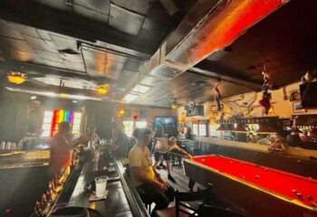 Bobby's Monkey Bar interior, a popular gay bar in Key West, Florida. People at bar, pool table, rainbow flag. Gay travel advice.