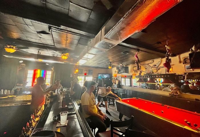 Bobby's Monkey Bar interior, a popular gay bar in Key West, Florida. People at bar, pool table, rainbow flag. Gay travel advice.