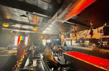 Bobby's Monkey Bar interior, a popular gay bar in Key West, Florida. People at bar, pool table, rainbow flag. Gay travel advice.