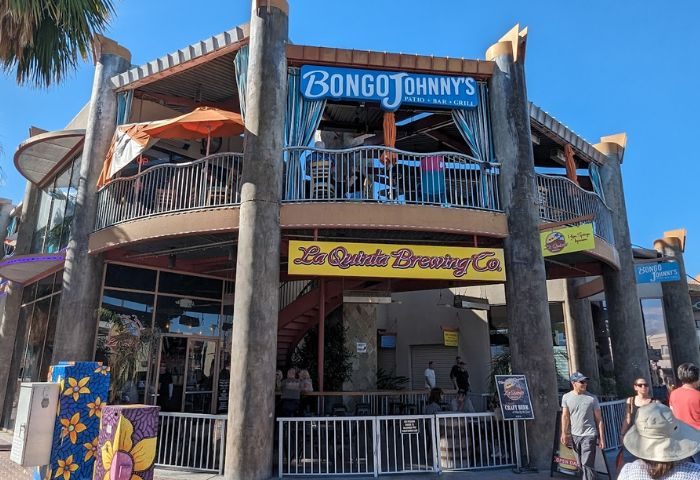 Bongo Johnny's Patio Bar & Grill exterior. Outdoor dining, patio, and bar scene. Popular gay travel destination. La Quinta Brewing Co. visible.