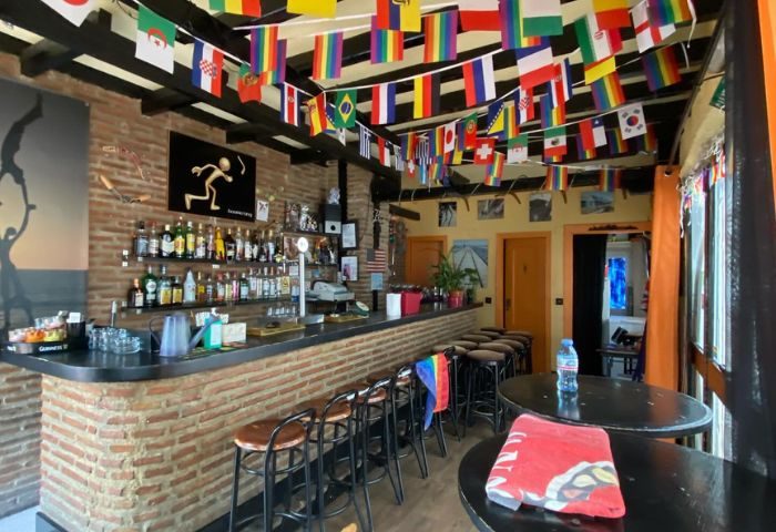 Interior of Boomerang Gay Bar in Torremolinos. Flags hang above the bar. Stools line the bar. Gay travel advice.