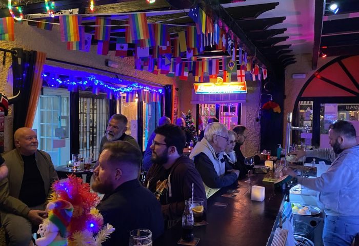 Boomerang Gay Bar in Torremolinos. Interior view with patrons at the bar, rainbow flags, and festive decorations. Gay travel destination.
