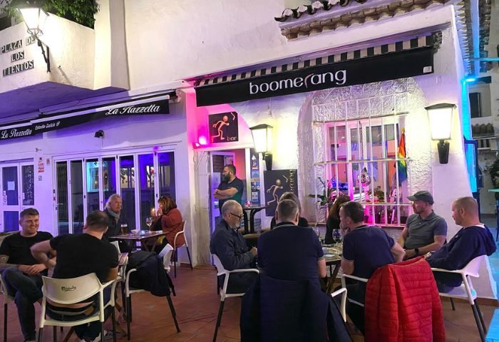 Boomerang Gay Bar in Torremolinos: Outdoor seating area with gay men. Rainbow flag visible. Nightlife scene, gay travel.