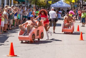 Key West gay travel: Men in pink shopping cart cars race on Bourbon St. during a fun event with live music and a cheering crowd.