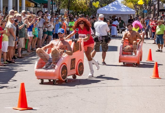 Key West gay travel: Men in pink shopping cart cars race on Bourbon St. during a fun event with live music and a cheering crowd.