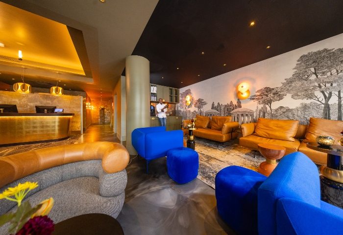 Boutique Hotel Albus Amsterdam Centre lobby. Stylish interior, gay-friendly hotel. Lounge area with blue velvet seating, leather sofas, and reception desk.