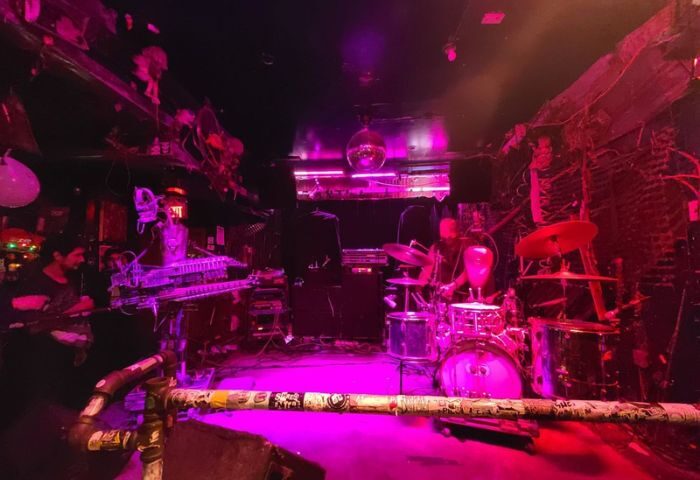 Live music at Bovine Sex Club, Toronto. Band on stage with drums, keyboard, and guitar under pink lighting. Gay travel nightlife.
