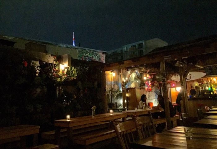 Night view of Bovine Sex Club's patio in Toronto. Outdoor seating, bar area, and CN Tower in the background. Gay travel destination.