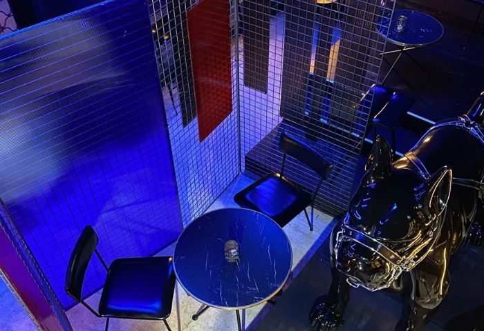 Interior of Boxer Cafe Bar, a gay bar in Barcelona. Features a table with chairs and a bulldog statue, with blue lighting.