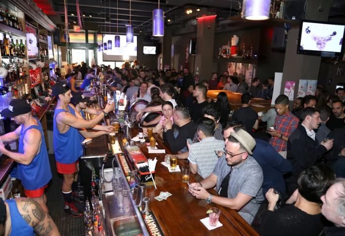 Crowded Boxers NYC gay sports bar. Bartenders in tank tops serve drinks. A popular gay bar for men in New York City.