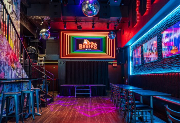 Boxers NYC gay bar interior. Stage, tables, and rainbow neon sign. Gay travel destination in New York City. Nightlife spot for gay men.