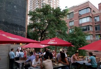 Boxers NYC HK in New York: Outdoor patio scene with gay men at tables under red umbrellas. Urban setting, travel advice.