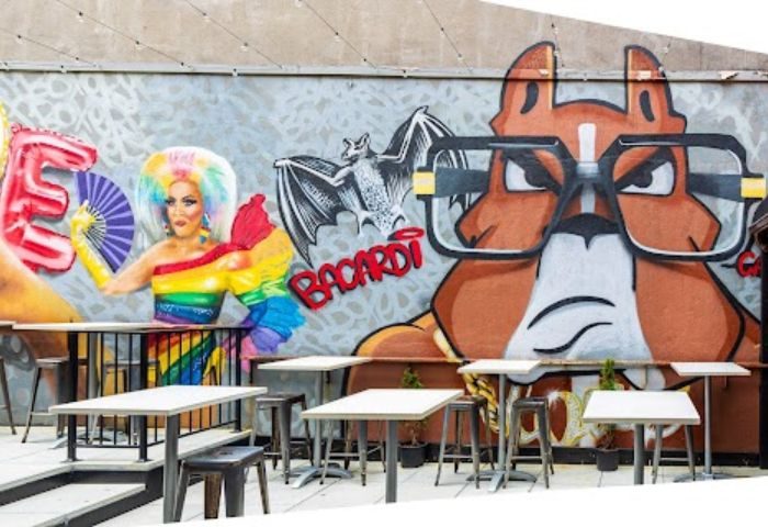 Boxers NYC HK in New York: Outdoor seating area with a mural featuring a drag queen in rainbow attire and a cartoon dog with glasses.