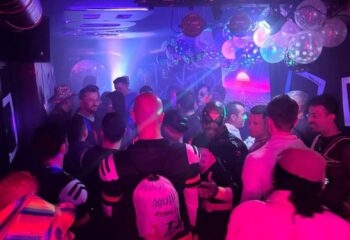 Gay bar in Sitges: Crowd of men enjoying drinks and music under disco lights. Nightlife scene for gay travelers.