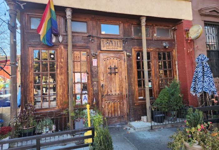 Branded Saloon, a gay bar in New York. Rustic wooden facade with rainbow flag. A welcoming spot for gay men's travel adventures.