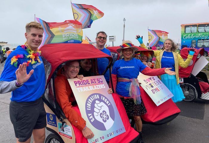 Brighton & Hove Pride 2024: Cheerful group at parade with rainbow flags and signs. Celebrating LGBTQ+ pride. Gay travel advice.