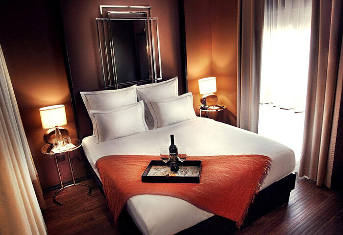 Brown TLV Hotel room, a top gay hotel in Tel Aviv near Shpagat gay bar. Wine bottle and glasses on the bed, lamps on bedside tables.