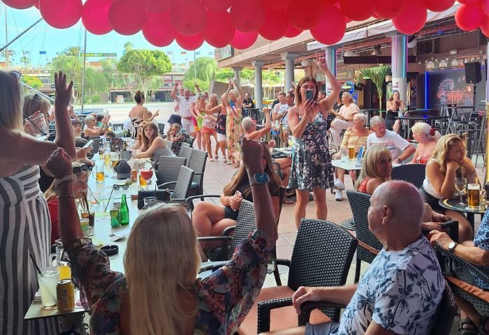 Buddies Bar, a Gran Canaria gay bar, is lively. People are dancing, drinking, and having fun under pink balloons. Outdoor seating area.
