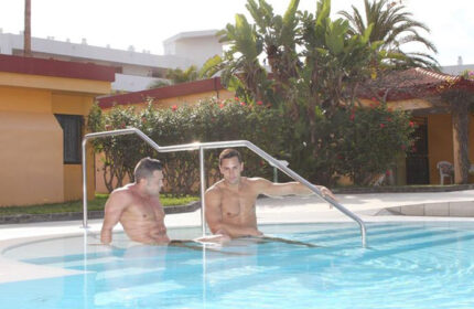 Bungalows Tenesoya gay men only hotel pool in Gran Canaria near Yumbo Center. Two shirtless men relaxing in the water on vacation.