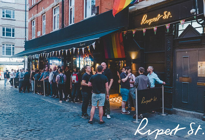 Crowd outside Rupert Street Bar, the busiest gay bar in Soho, London. Rainbow flag visible. Gay travel advice.