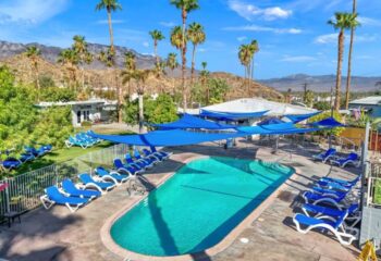 CCBC Resort Hotel pool in Palm Springs. Blue sunshades, lounge chairs, palm trees, and mountains in the background. Gay travel.