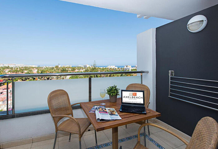 AxelBeach Maspalomas balcony view. Apart & Lounge Club for adults. Laptop, chairs, table, and ocean view. CHEAP apartments for gay men travel.