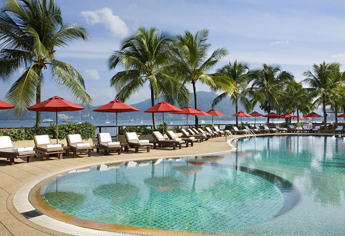 Amari Phuket, Thailand: Beachfront pool at LGBT-friendly hotel near Patong. Palm trees, red umbrellas, and lounge chairs by the pool.