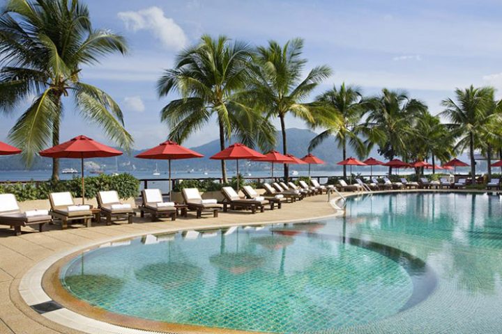 Amari Phuket, Thailand: Beachfront pool at LGBT-friendly hotel near Patong. Palm trees, red umbrellas, and lounge chairs by the pool.