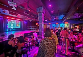 Montreal's Cabaret Mado gay bar: Drag show venue with a stage, purple lighting, and patrons enjoying the performance. Nightlife scene.
