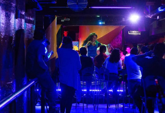 Cabaretito El Taller gay bar in Mexico. Patrons watch a performer on stage in a dimly lit room with blue lighting. Gay travel advice.