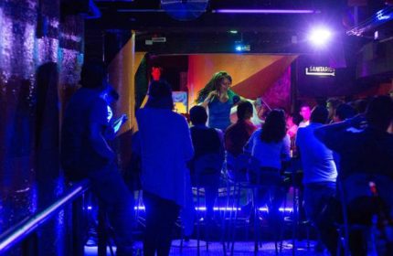Cabaretito El Taller gay bar in Mexico. Patrons watch a performer on stage in a dimly lit room with blue lighting. Gay travel advice.