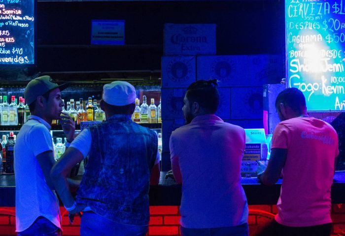 Cabaretito El Taller Gay Bar in Mexico: Men at the bar with drinks. Nightlife scene, gay travel. Neon lights, bar setting, socializing.