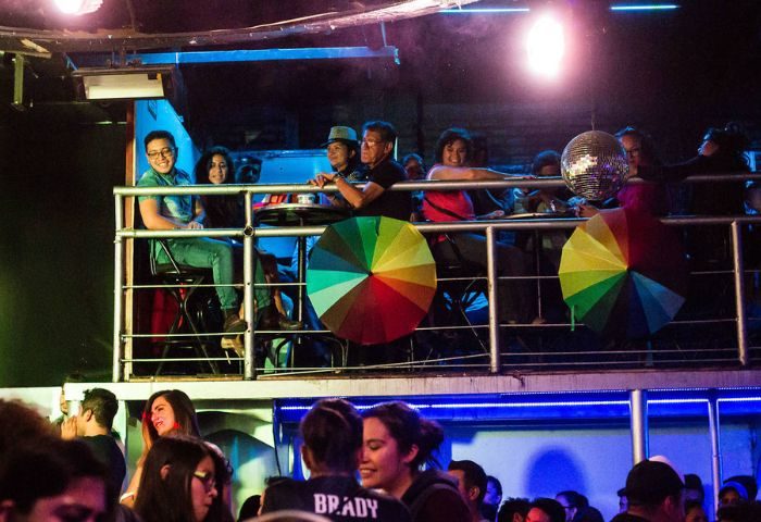 Cabaretito Fusion Gay Bar in Mexico: People on a balcony, rainbow umbrellas, disco ball, and crowd below in a lively gay bar atmosphere.